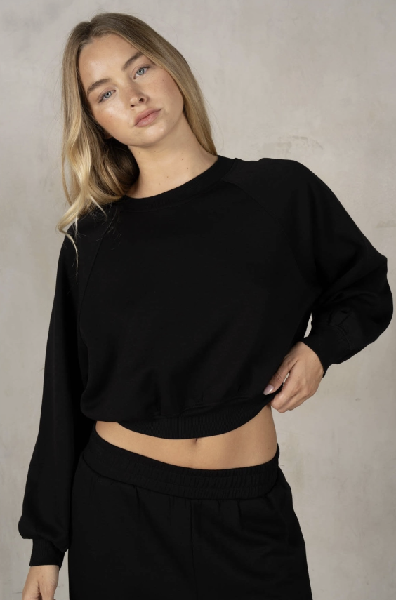 Person wearing a black sweater and black pants against a neutral background