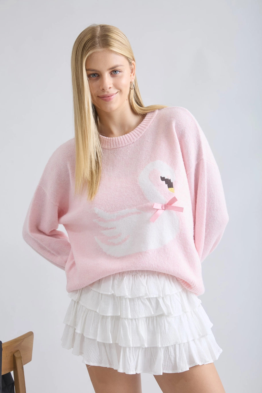 Woman wearing a pink sweater with a design and a white skirt on a plain background