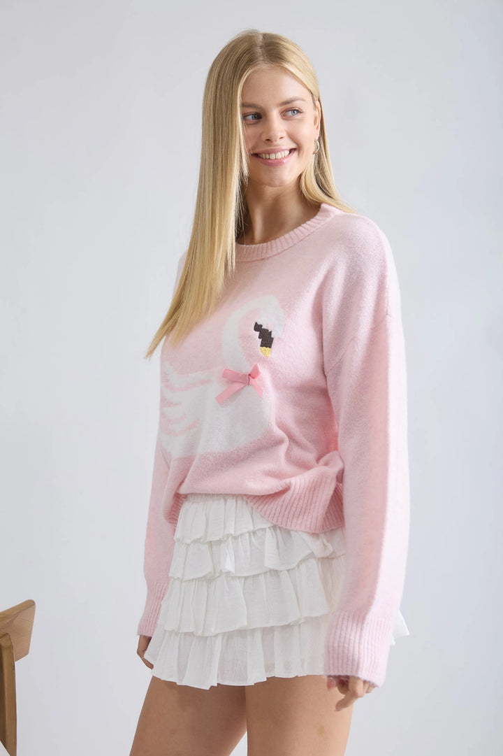 Woman wearing a pink sweater with a cartoon design and a white skirt on a plain background