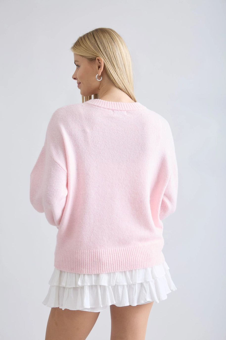 Woman wearing a pink sweater and white skirt on a plain background