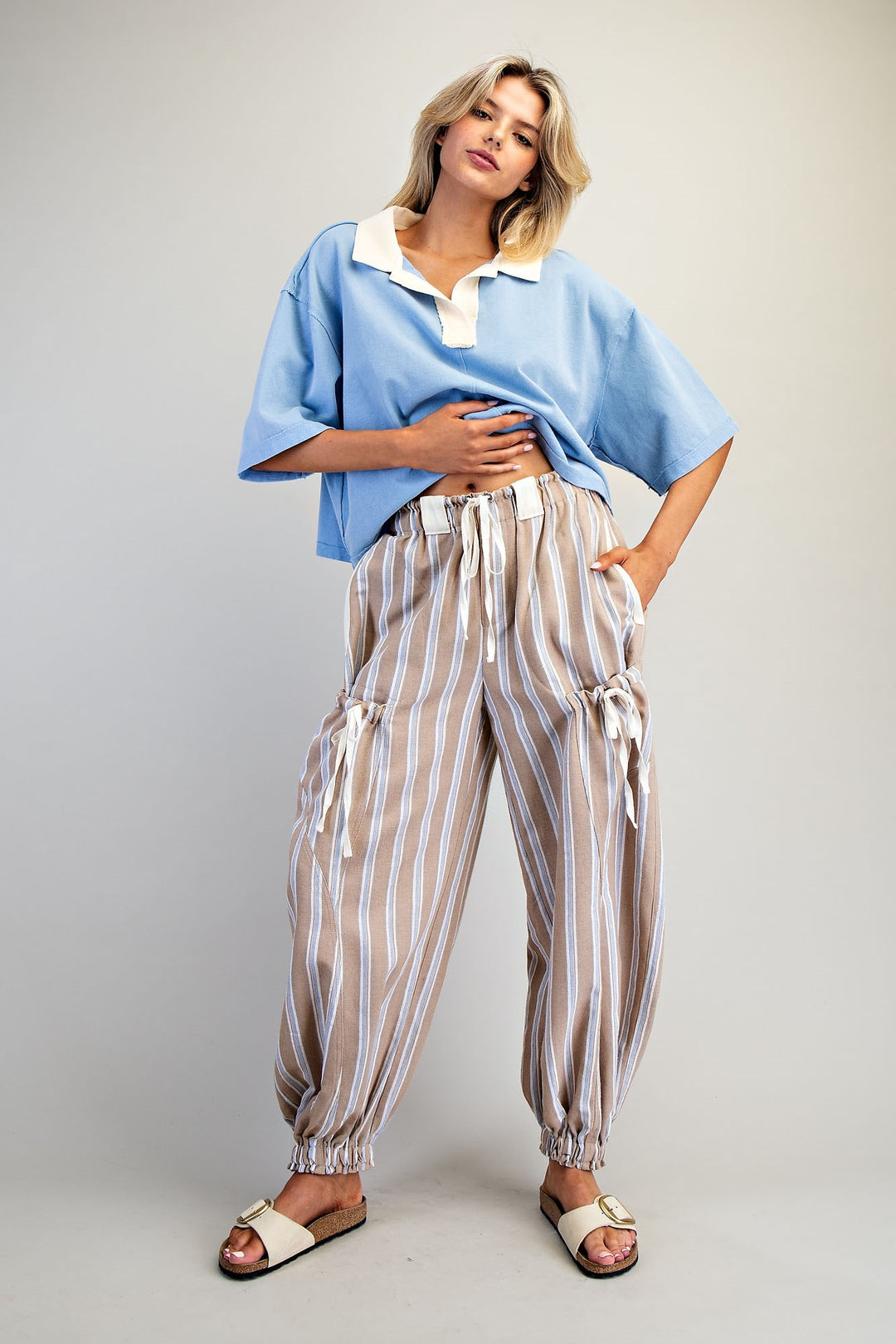 Woman wearing a blue top and striped pants against a plain background