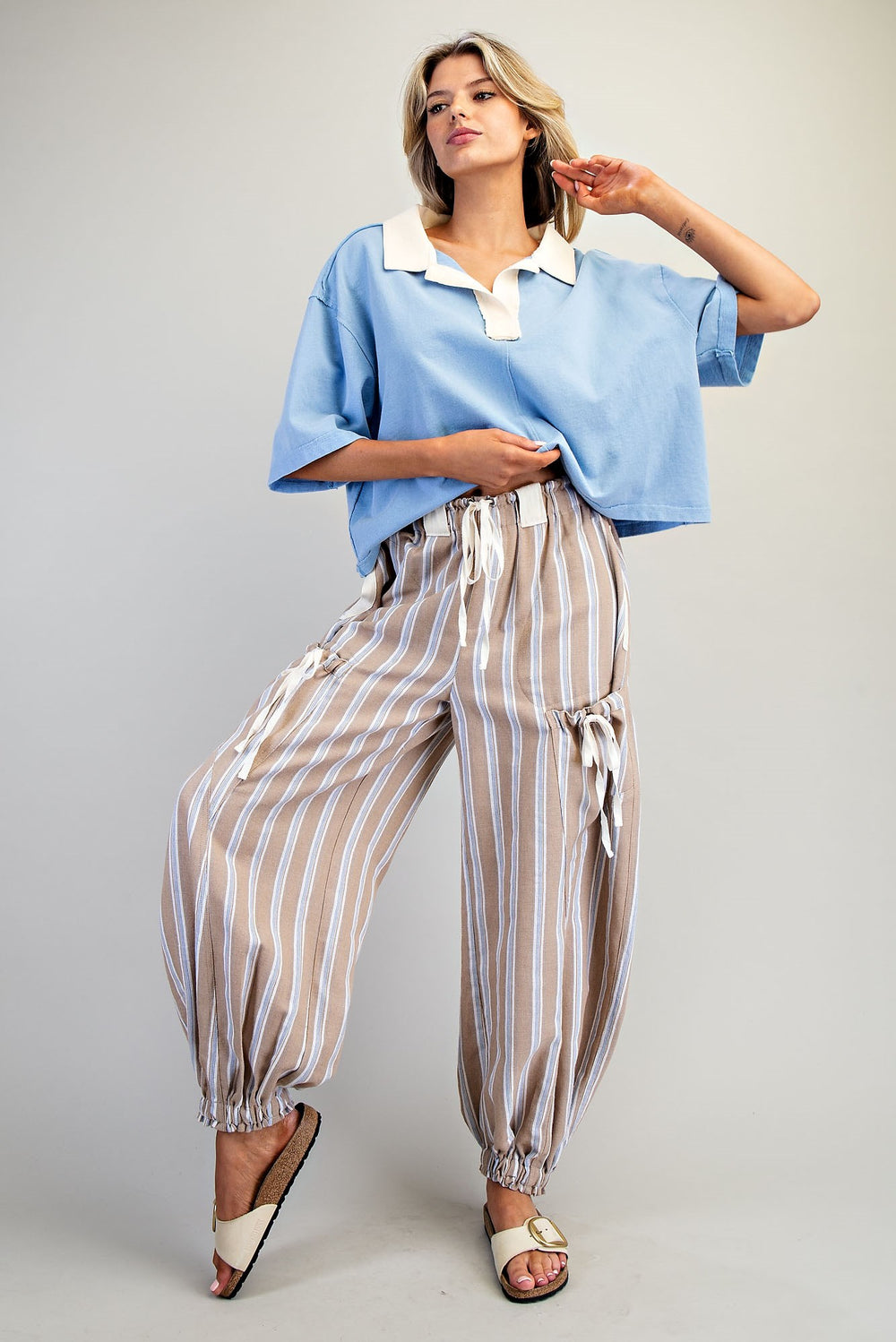 Woman wearing a light blue top and striped pants on a plain background