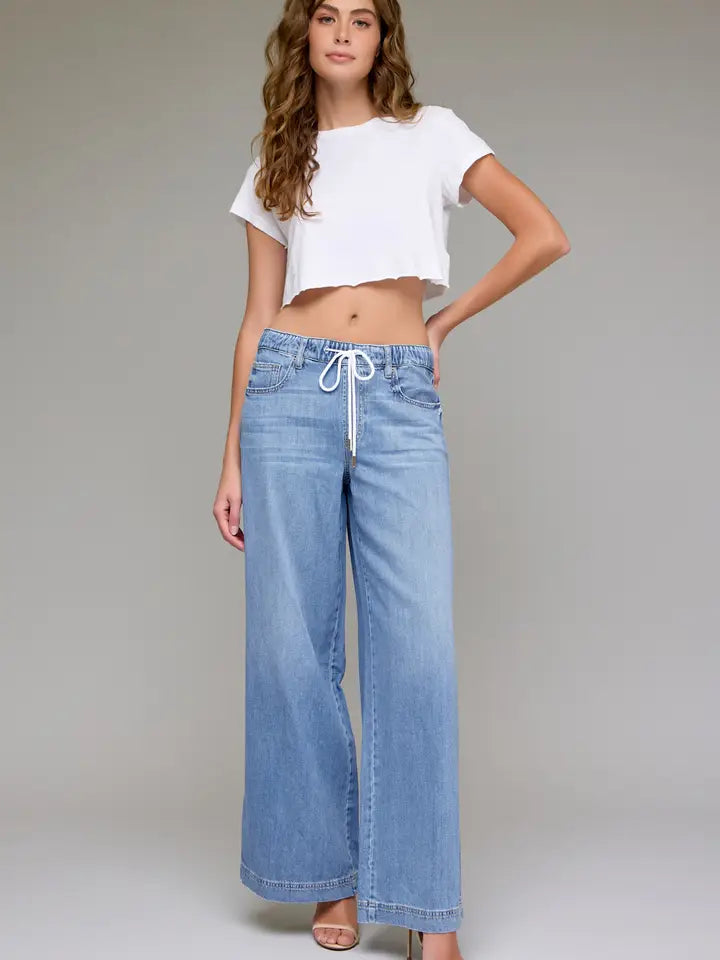 Woman wearing a white crop top and blue jeans on a plain background