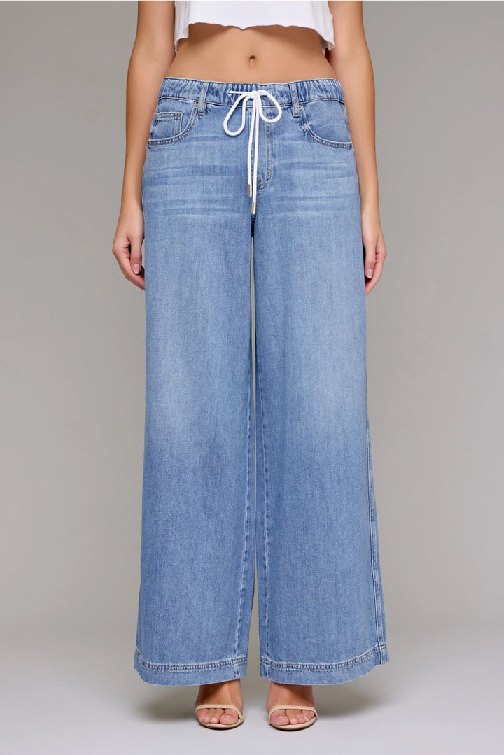 Wide-leg denim pants with a drawstring waist on a plain background