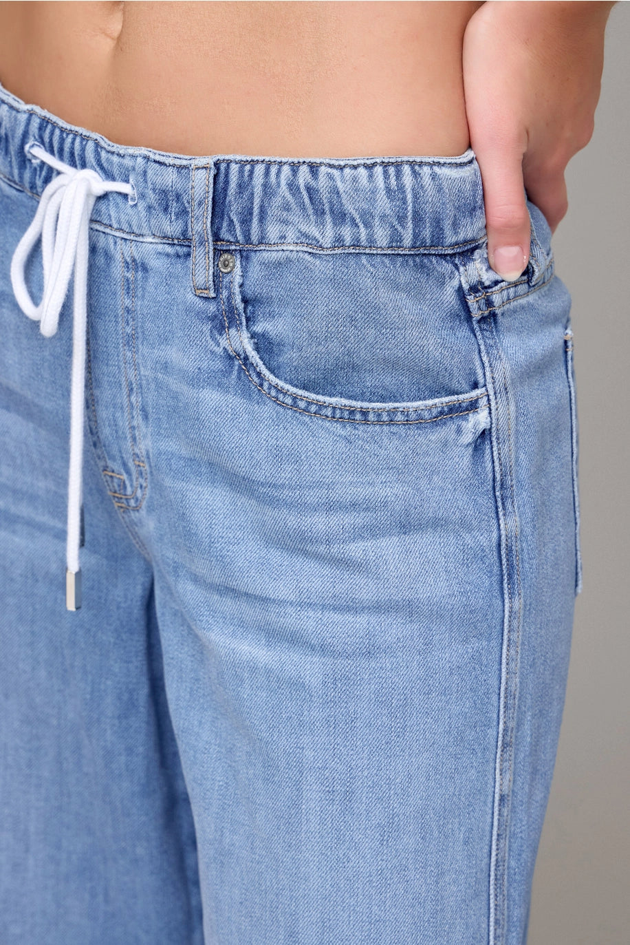Close-up of light blue jeans with a drawstring on a neutral background