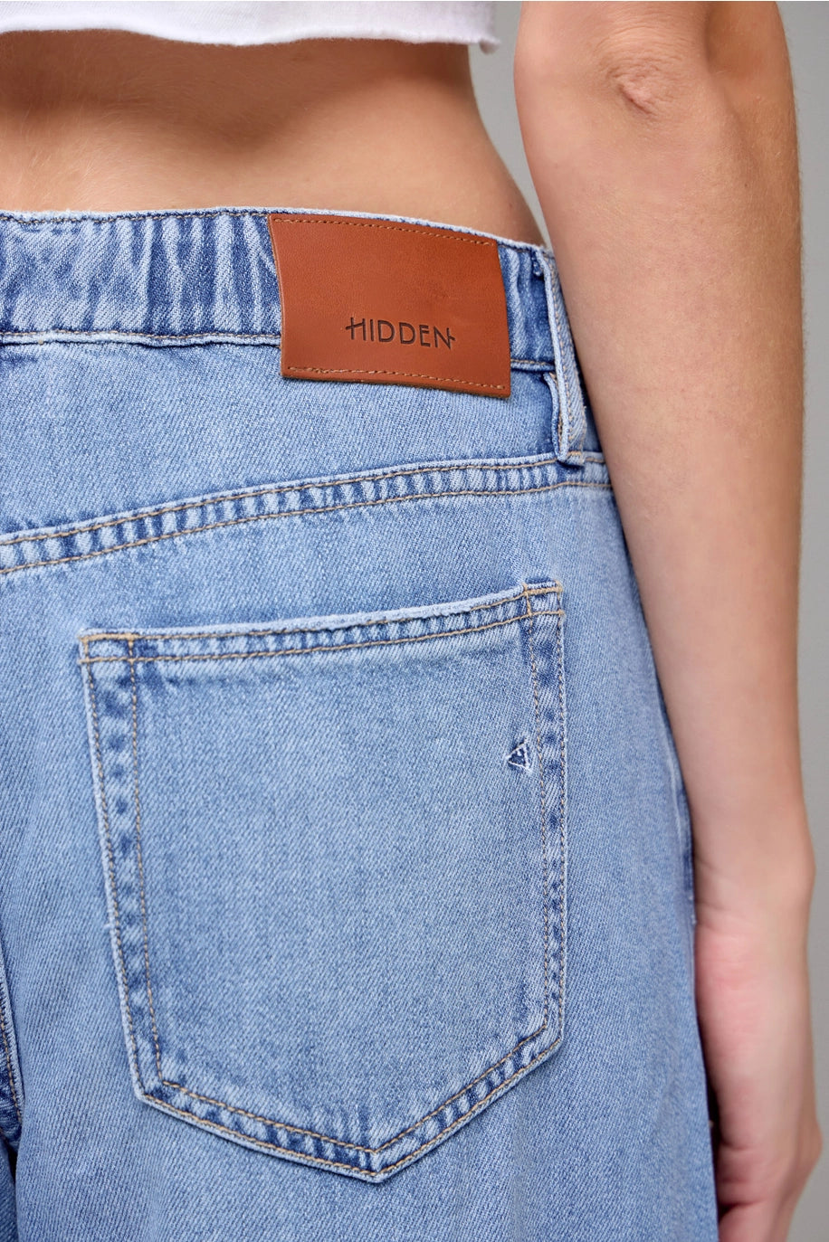 Close-up of a person wearing light blue jeans with a brown leather label on the back pocket.