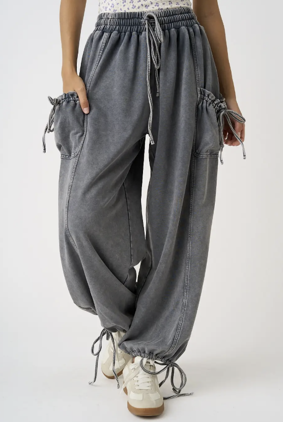 A person wearing loose, faded gray drawstring harem-style pants with side pockets and drawstring ankle cuffs, paired with white sneakers against a plain light background.