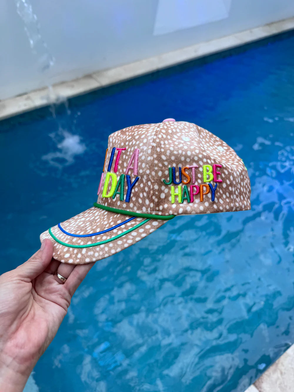 Cap with colorful text held by a hand in front of a pool