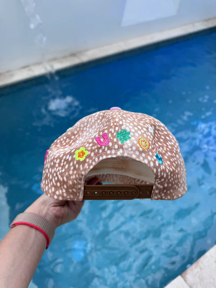 Cap with colorful floral designs held in front of a pool