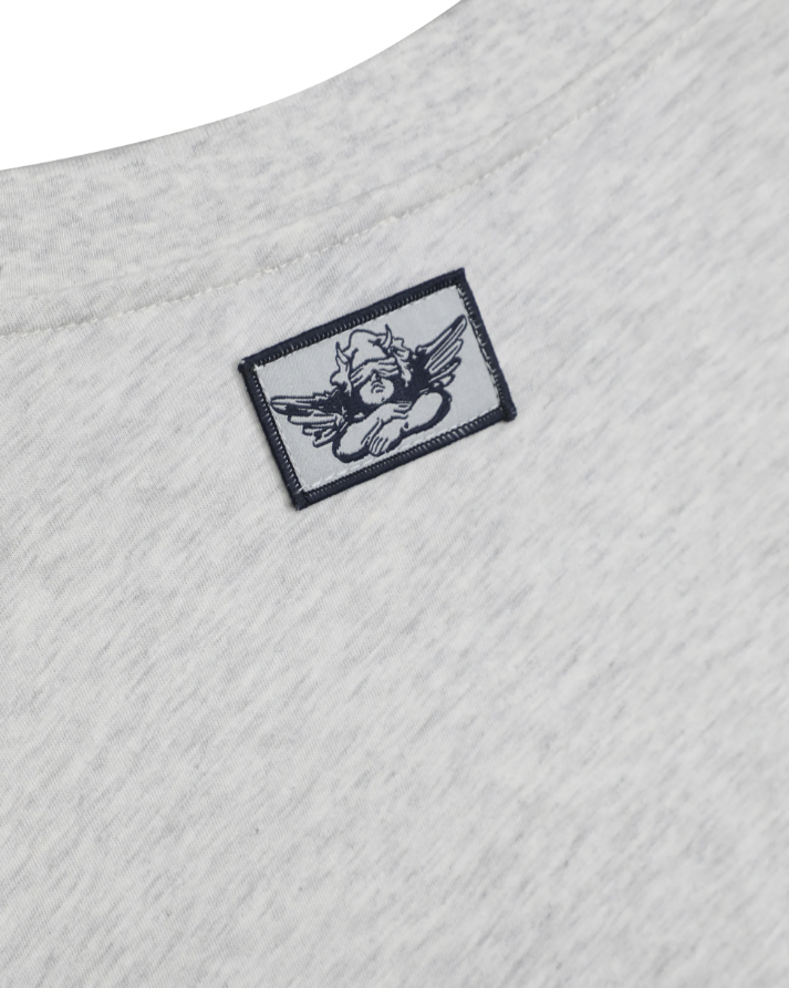 Close-up of a light heather gray t-shirt showing a small rectangular embroidered patch on the chest with a black angel illustration.