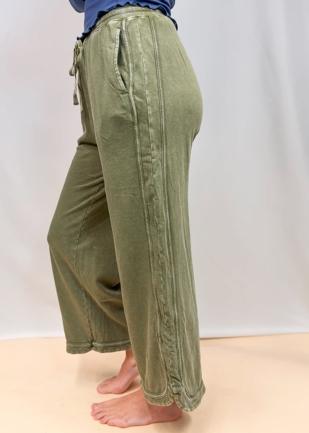 Woman shown from side view wearing green sweatpants on plain background