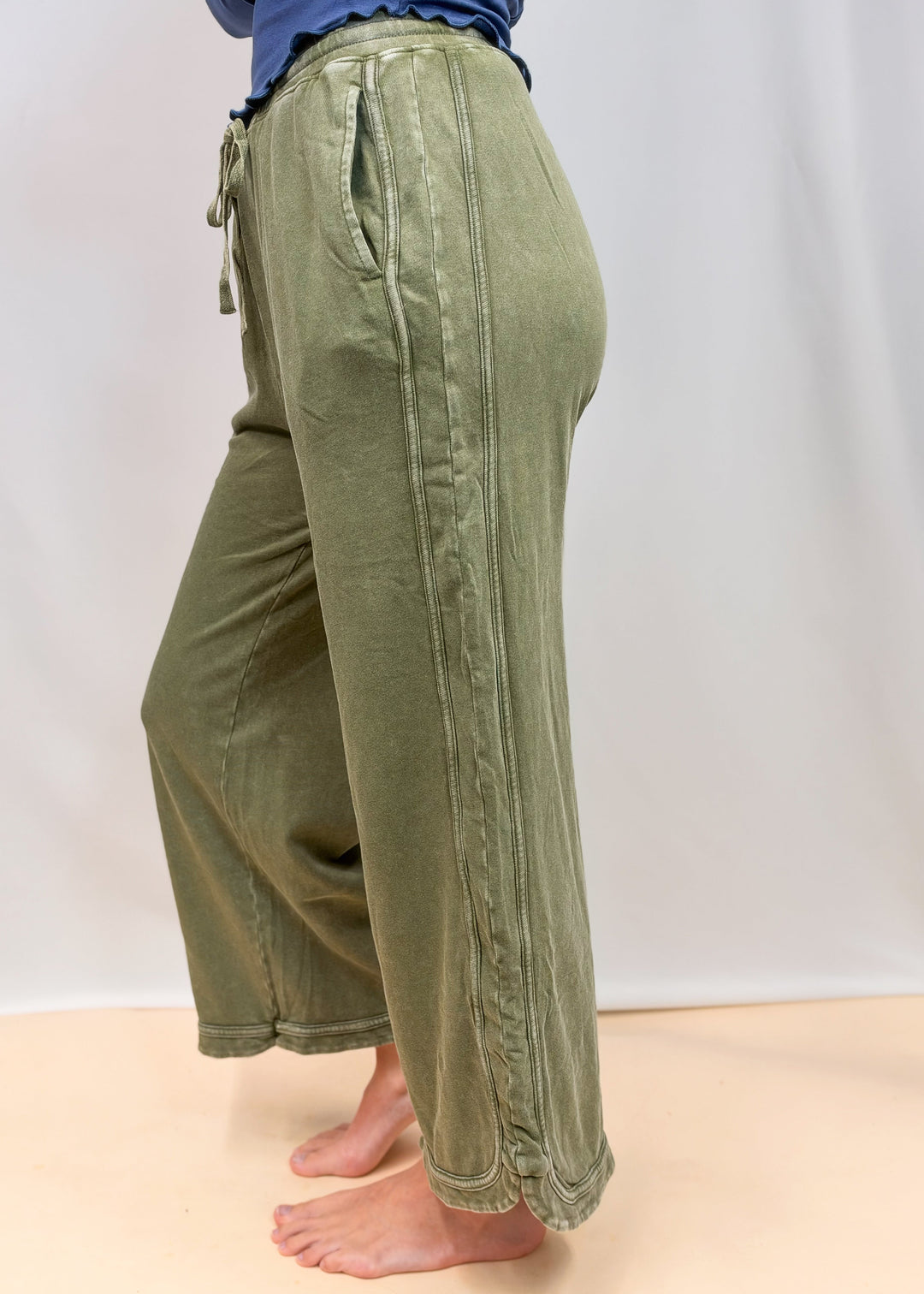 Woman shown from side view wearing green sweatpants on plain background