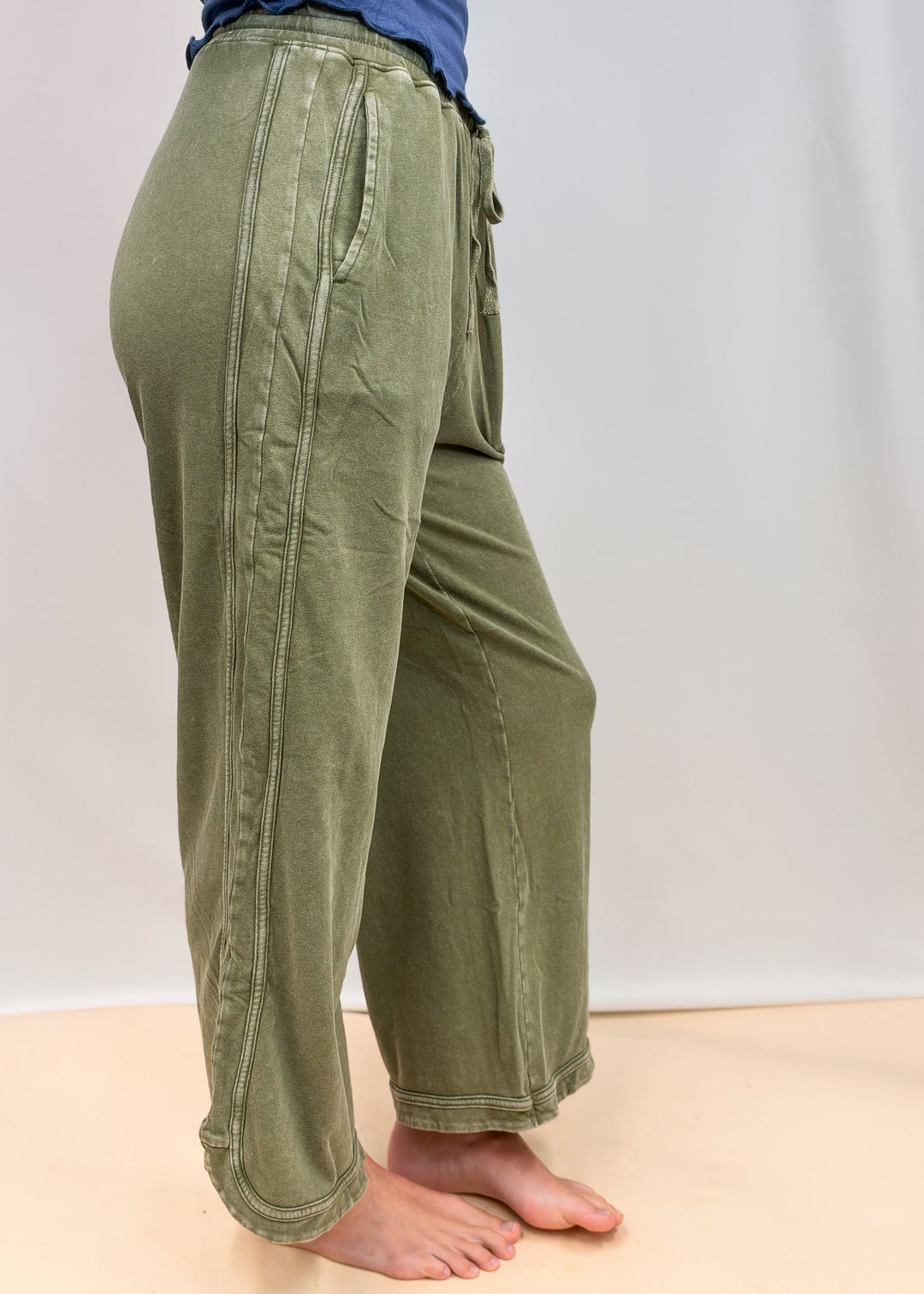 Woman shown from side view wearing green sweatpants on plain background