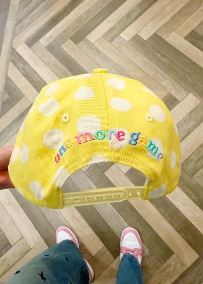 Yellow cap with white polka dots and colorful text on a wooden floor.