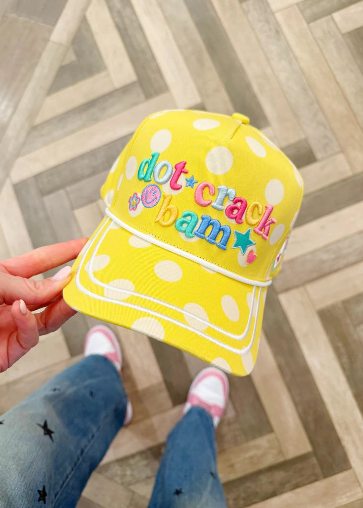 Yellow polka dot cap with colorful text held by a person on a wooden floor.