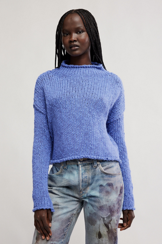 Person wearing a blue knitted sweater and light blue jeans on a plain background