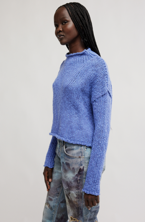 Person wearing a blue sweater and patterned pants on a plain background