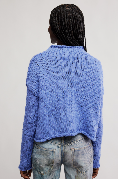 Person wearing a blue knitted sweater and jeans on a plain background