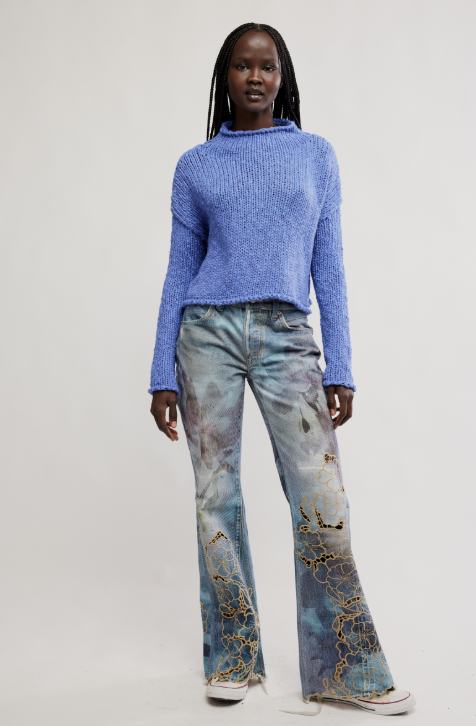 Person wearing a blue sweater and patterned jeans on a plain background