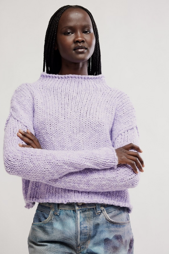 Person wearing a light purple sweater and jeans with arms crossed on a white background