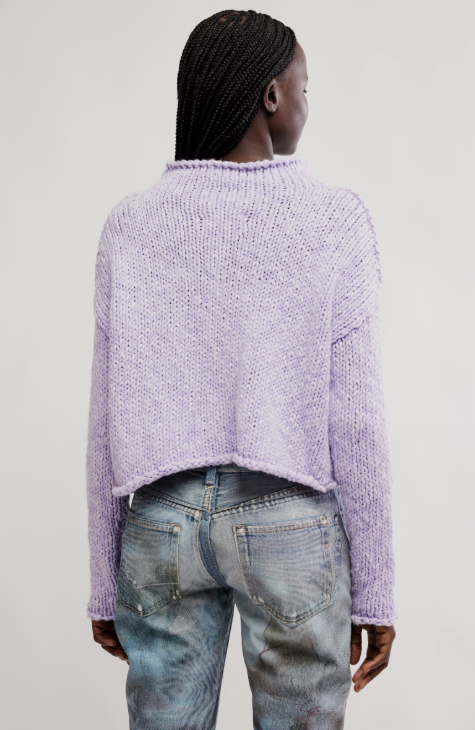 Person wearing a light purple sweater and blue jeans on a plain background