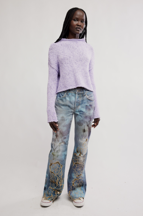 Person wearing a light purple sweater and patterned jeans on a white background
