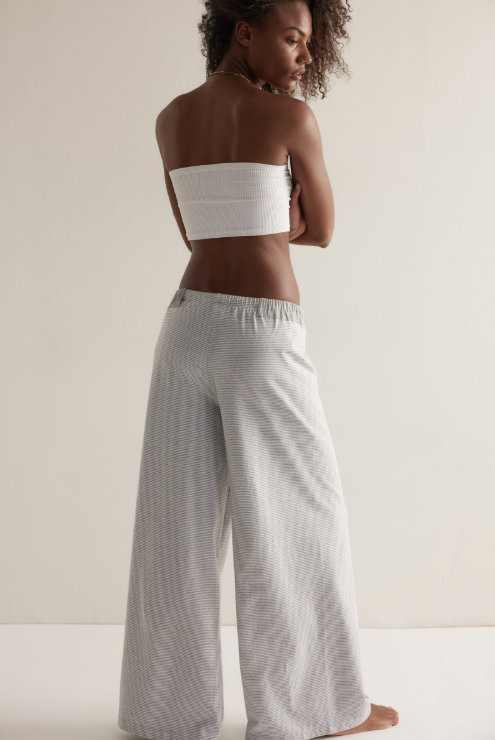 Woman wearing a white strapless top and light gray striped pants on a plain background