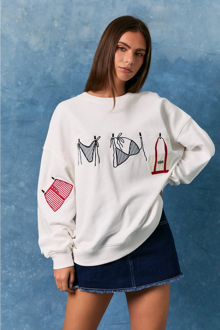 Woman wearing white sweatshirt with bathing suit graphics on plain background