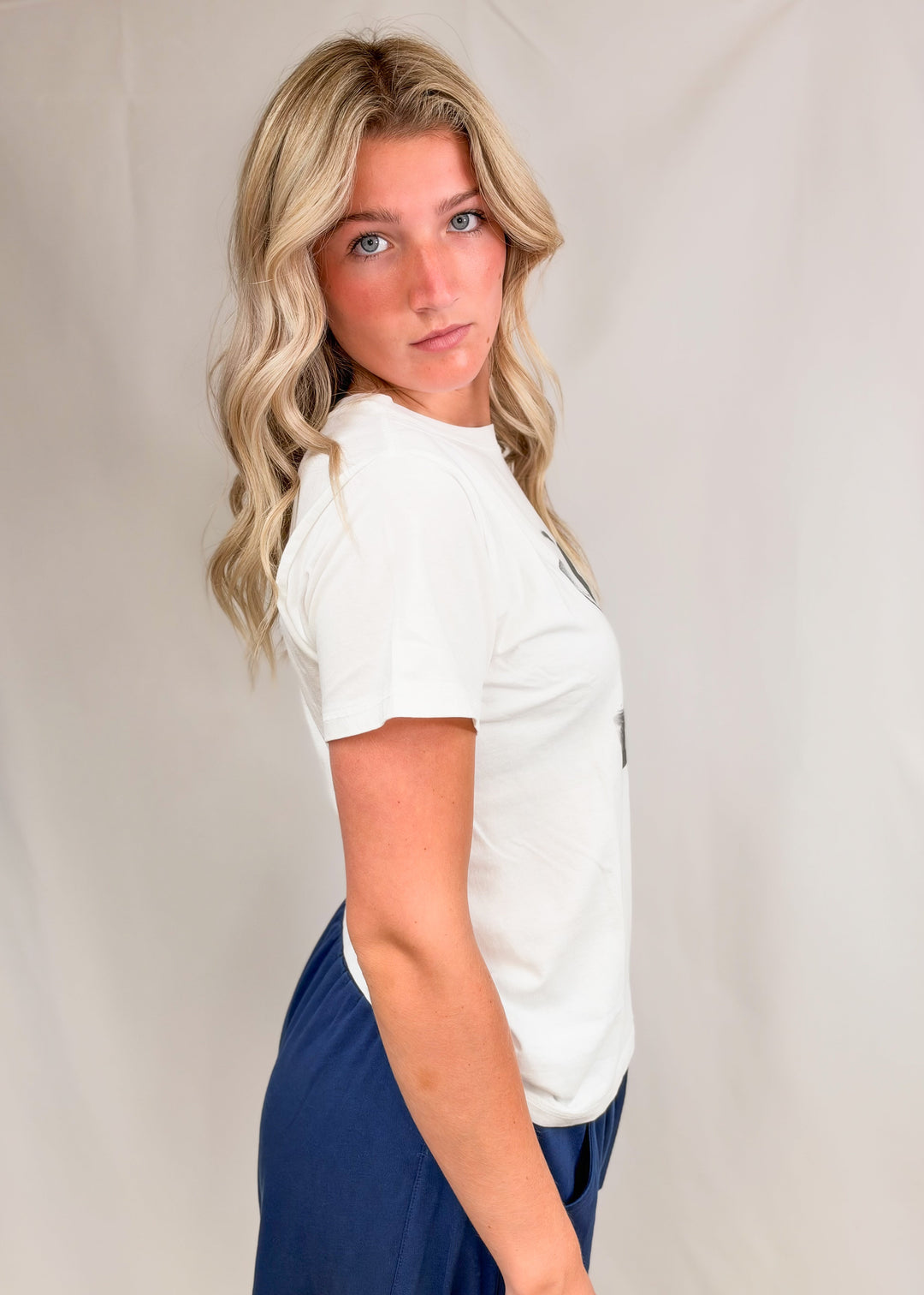 Woman shown from side wearing graphic tee and blue pants on plain background