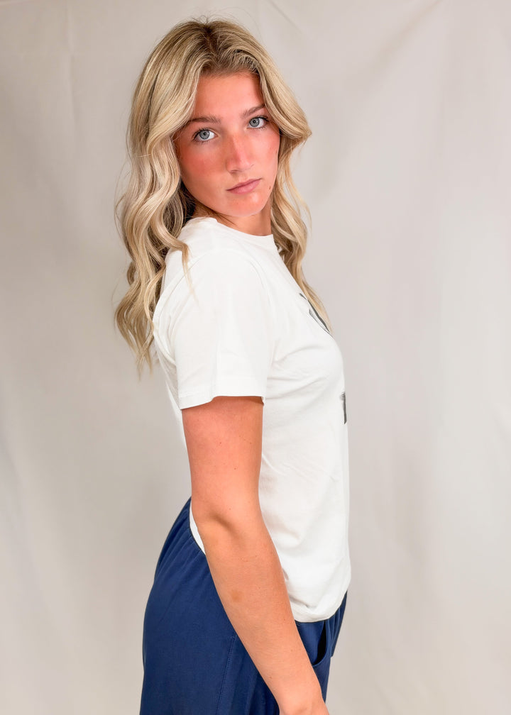 Woman shown from side wearing graphic tee and blue pants on plain background