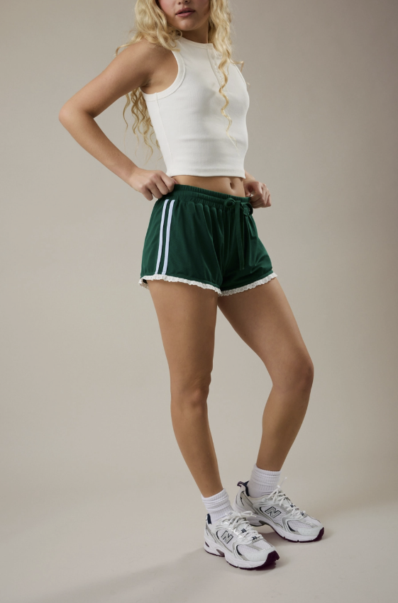 Person wearing a white crop top and green shorts with a white stripe on a beige background