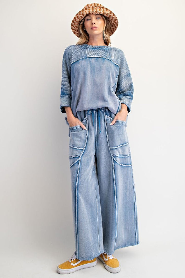 Woman wearing a denim outfit with wide-leg pants and a hat on a plain background