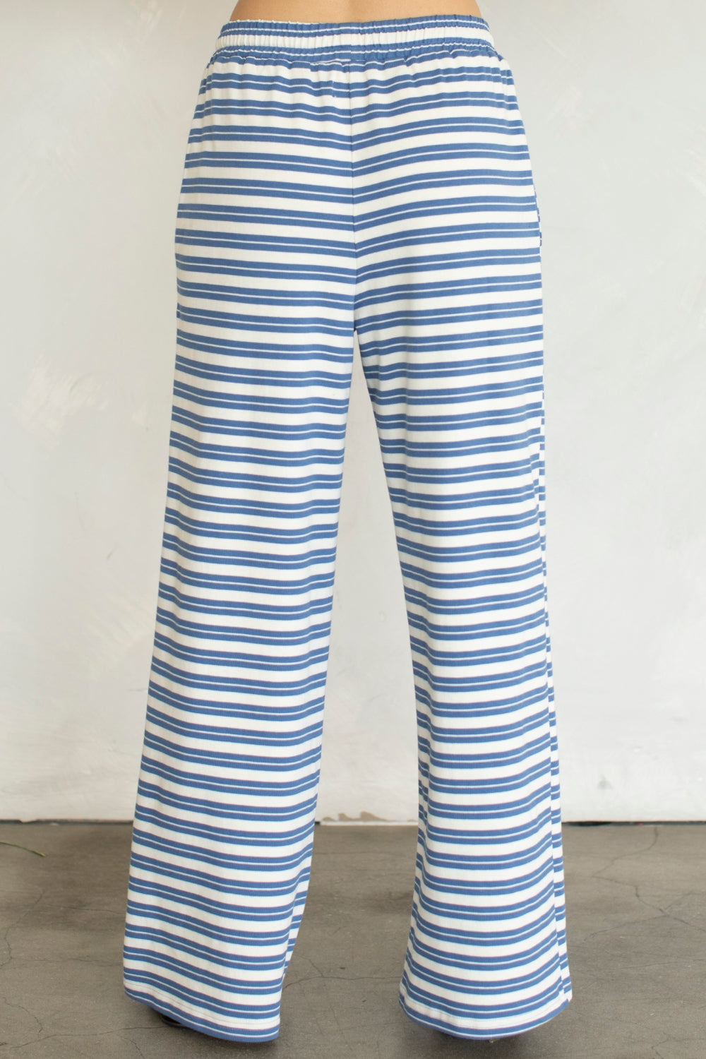 Back of woman wearing blue and white stripe pants on plain background