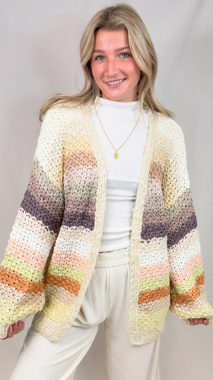 Woman wearing chunky knit cardigan with multi color stripes on plain background