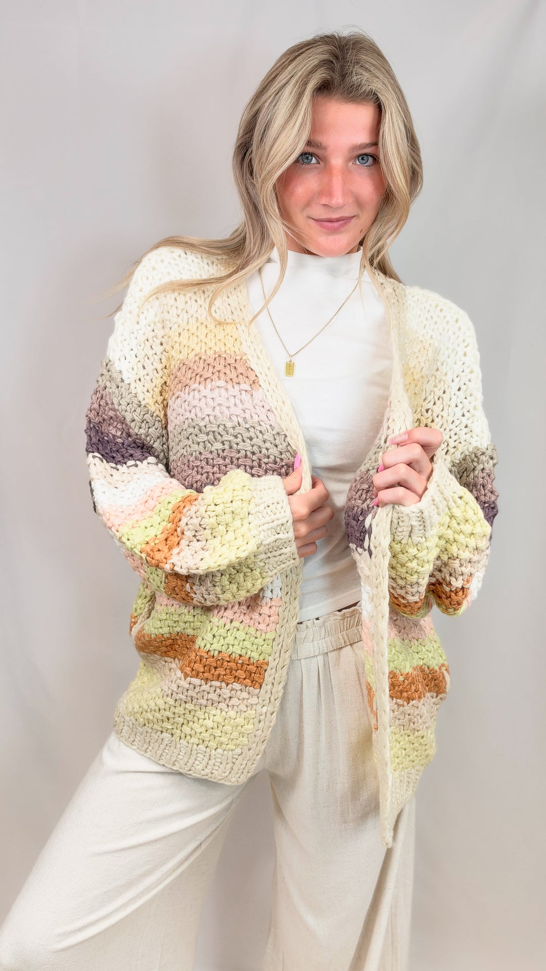 Woman wearing chunky knit sweater with multi color stripes on plain background