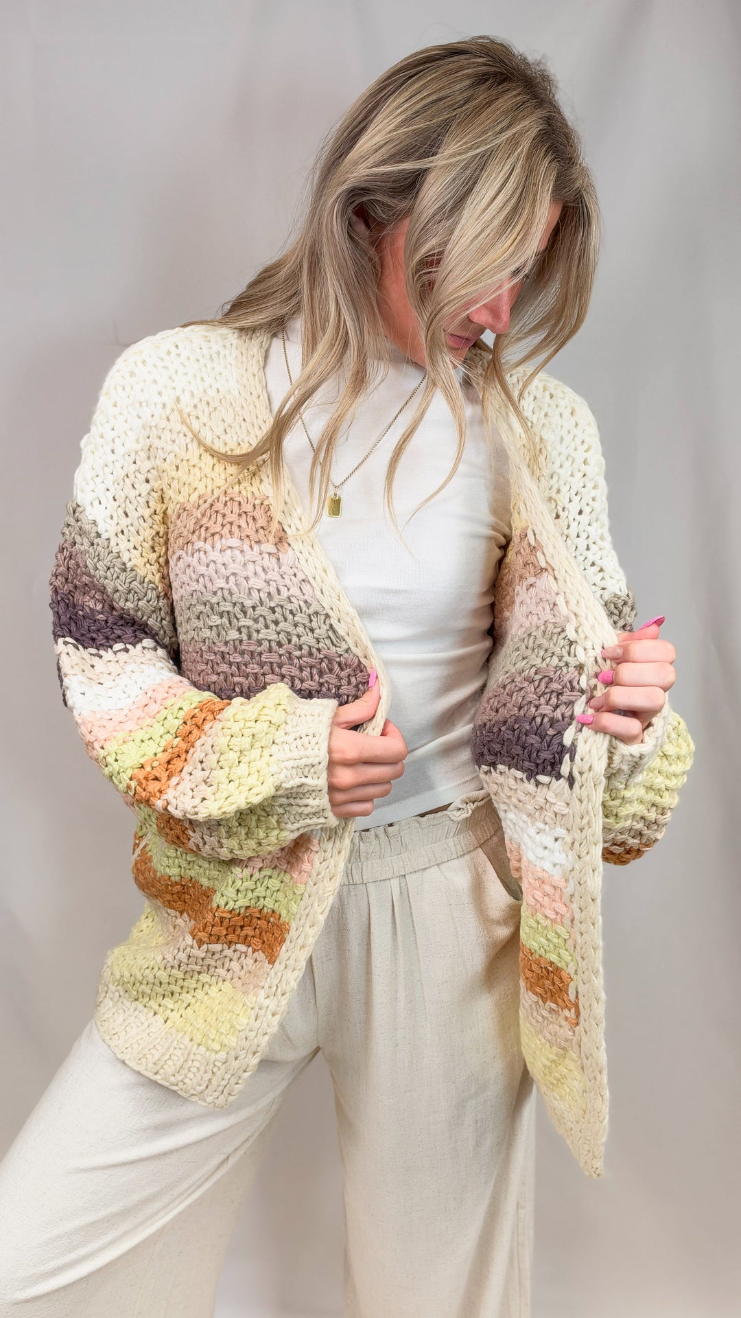 Woman wearing chunky knit sweater with multi color stripes on plain background