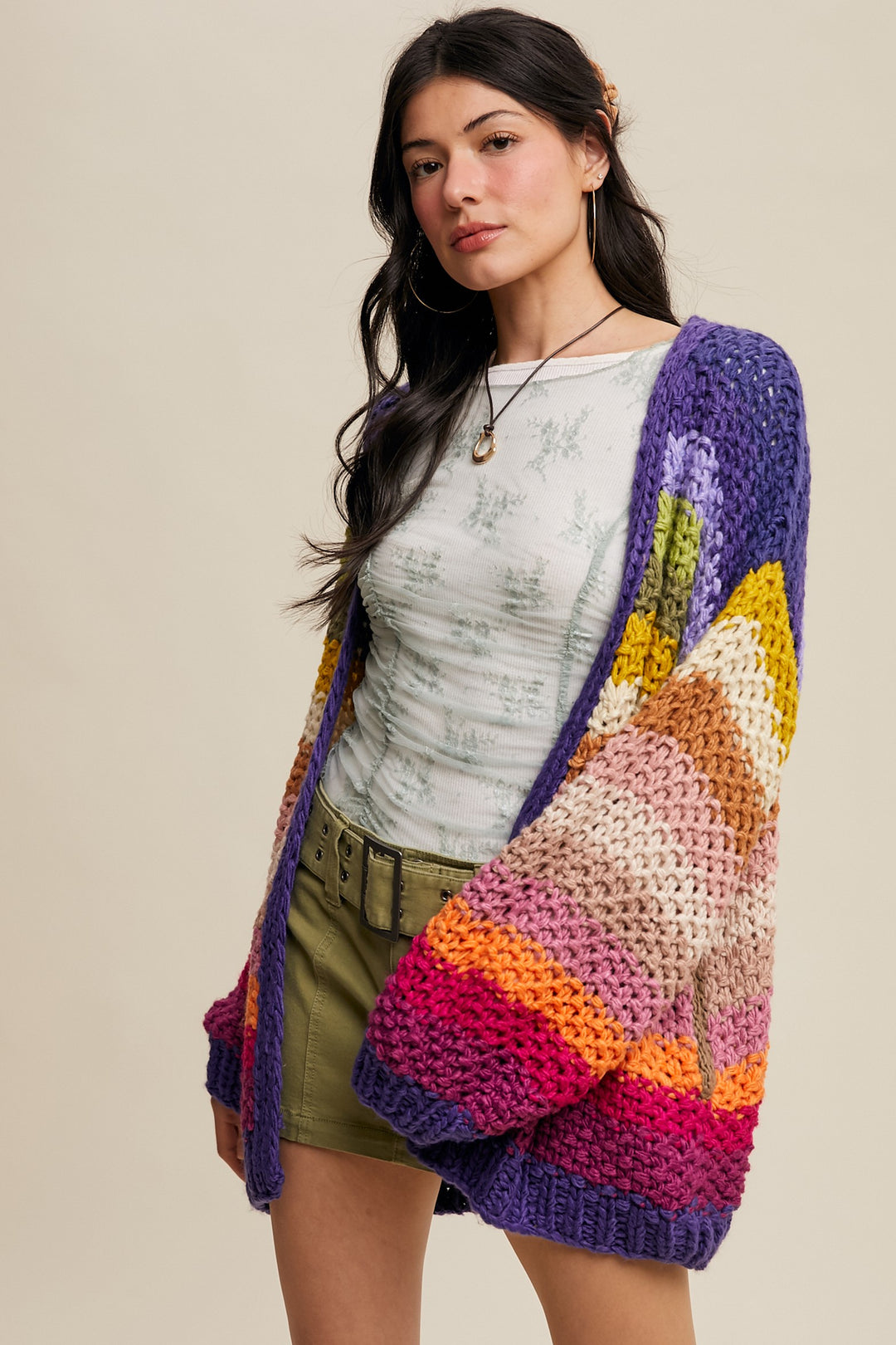 Woman wearing a colorful crocheted cardigan against a beige background