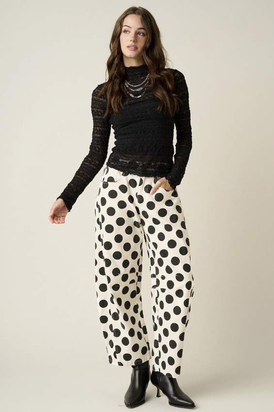 Woman wearing black and white polka dot pants with black top on plain background