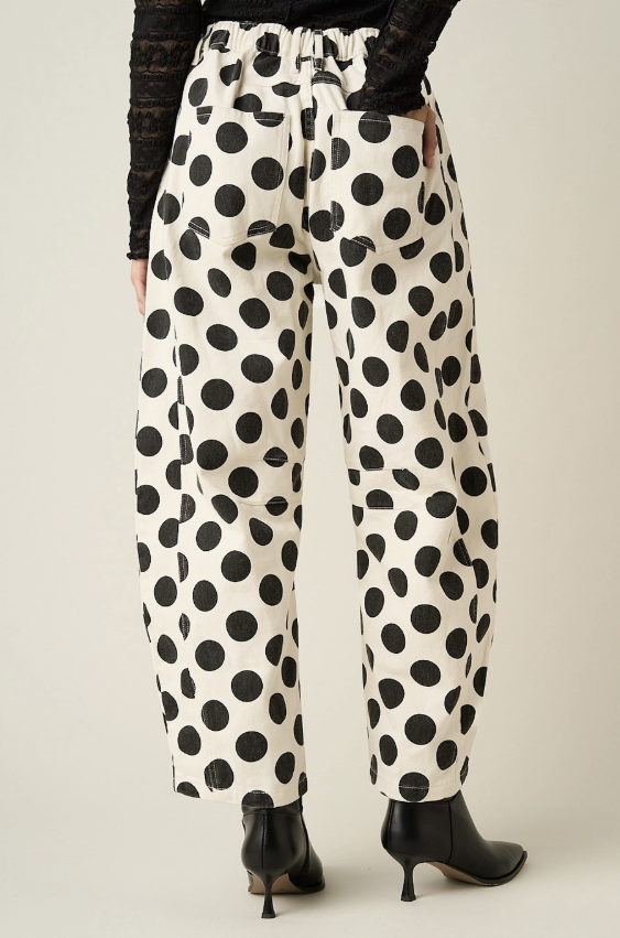 Woman shown from behind wearing black and white polka dot pants on plain background
