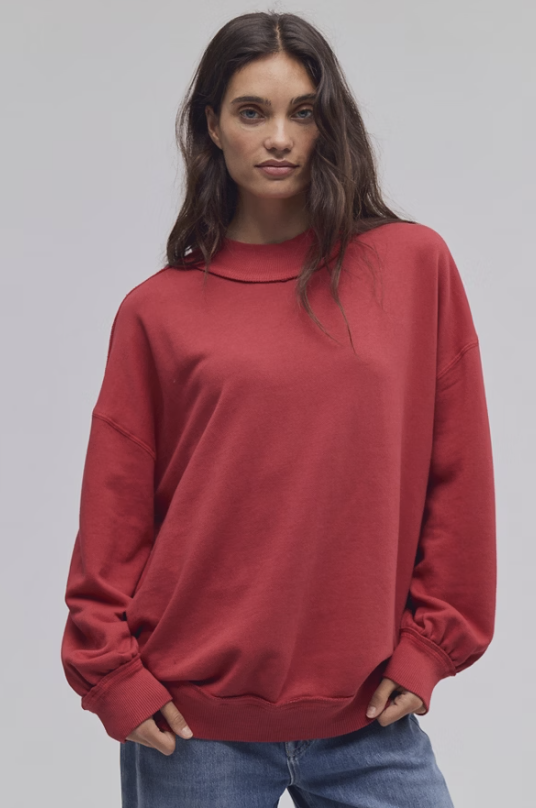 Woman wearing red mock neck sweatshirt with blue jeans on white background