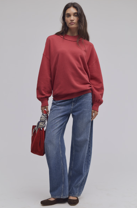 Woman wearing red mock neck sweatshirt and blue jeans on white background