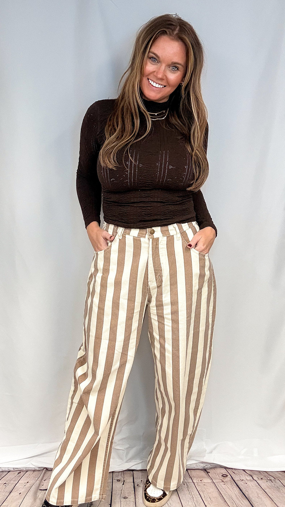 Woman wearing beige and white stripe pants with brown mock neck top on white background