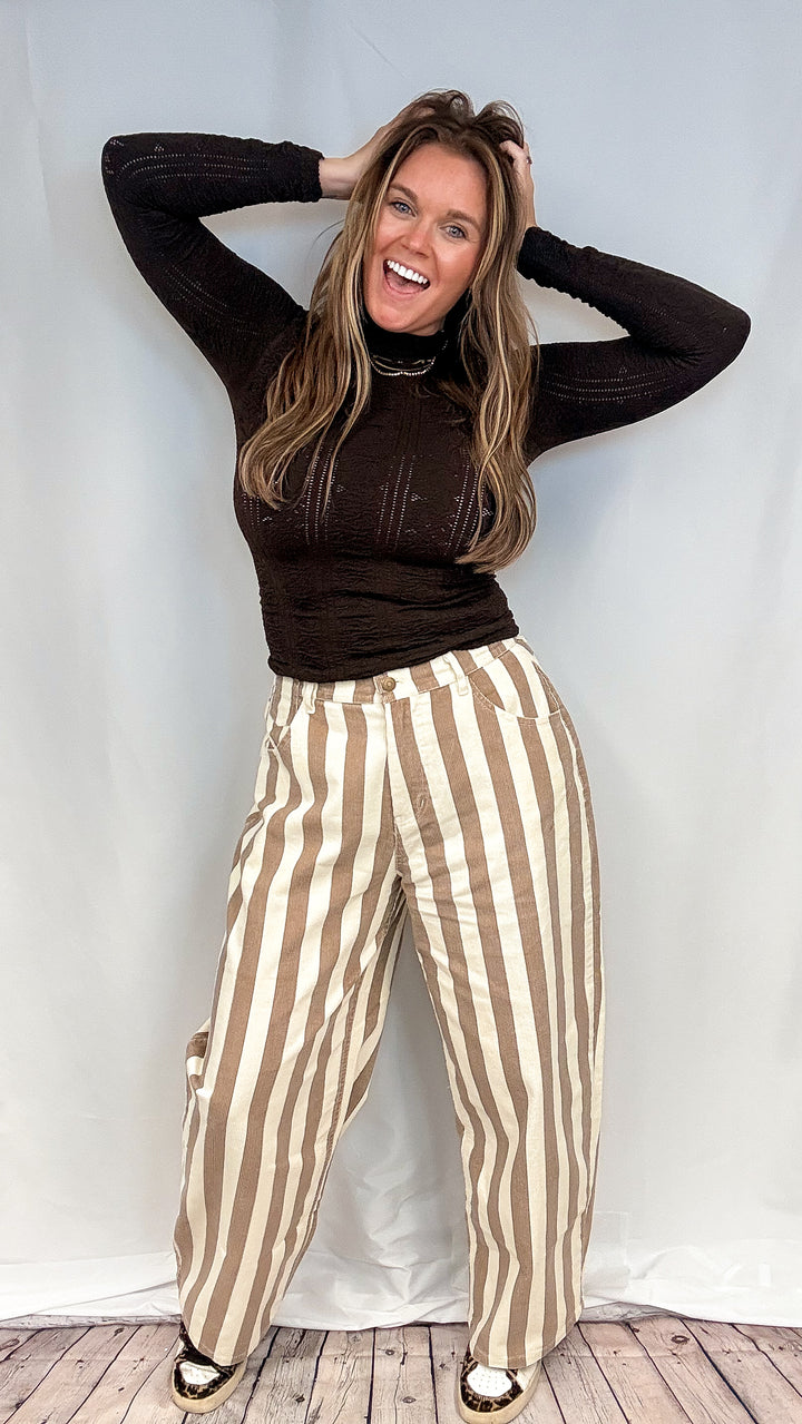 Woman wearing beige and white stripe pants with brown mock neck top on white background