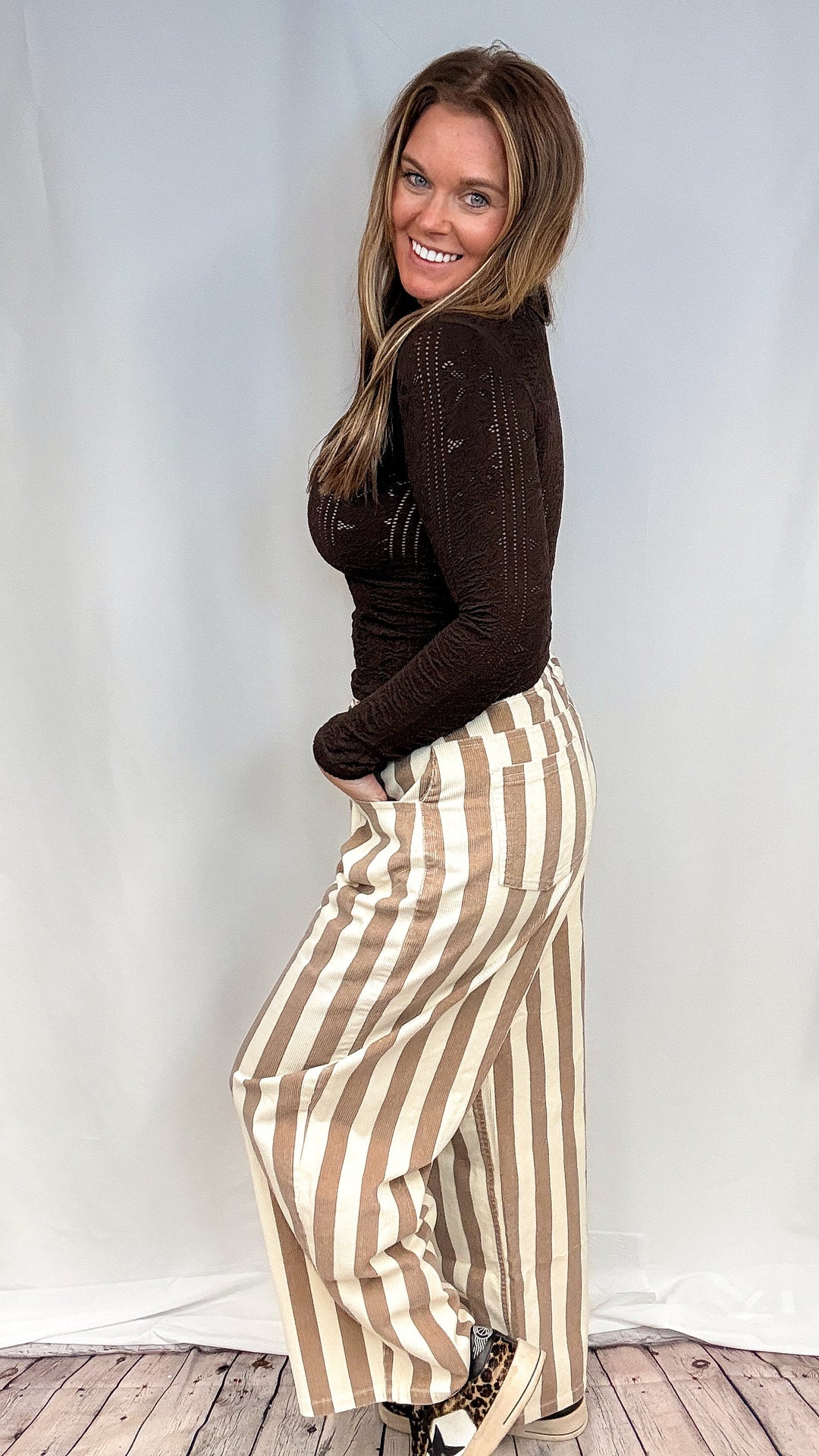 Woman wearing beige and white stripe pants with brown mock neck top on white background