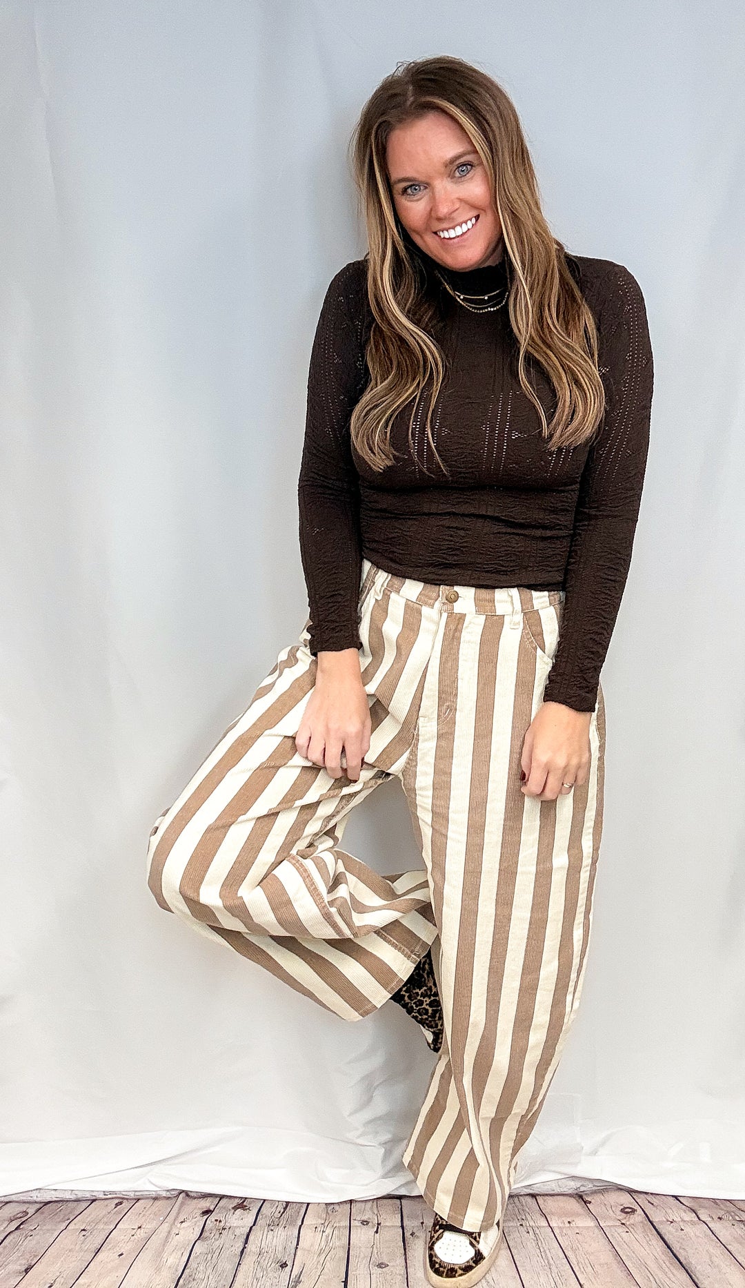 Woman wearing beige and white stripe pants and brown mock neck top on white background