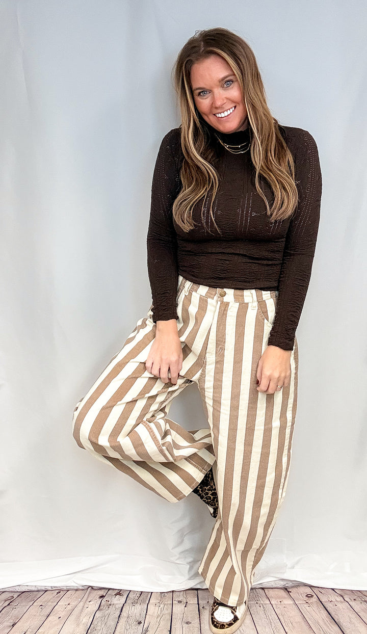 Woman wearing beige and white stripe pants and brown mock neck top on white background