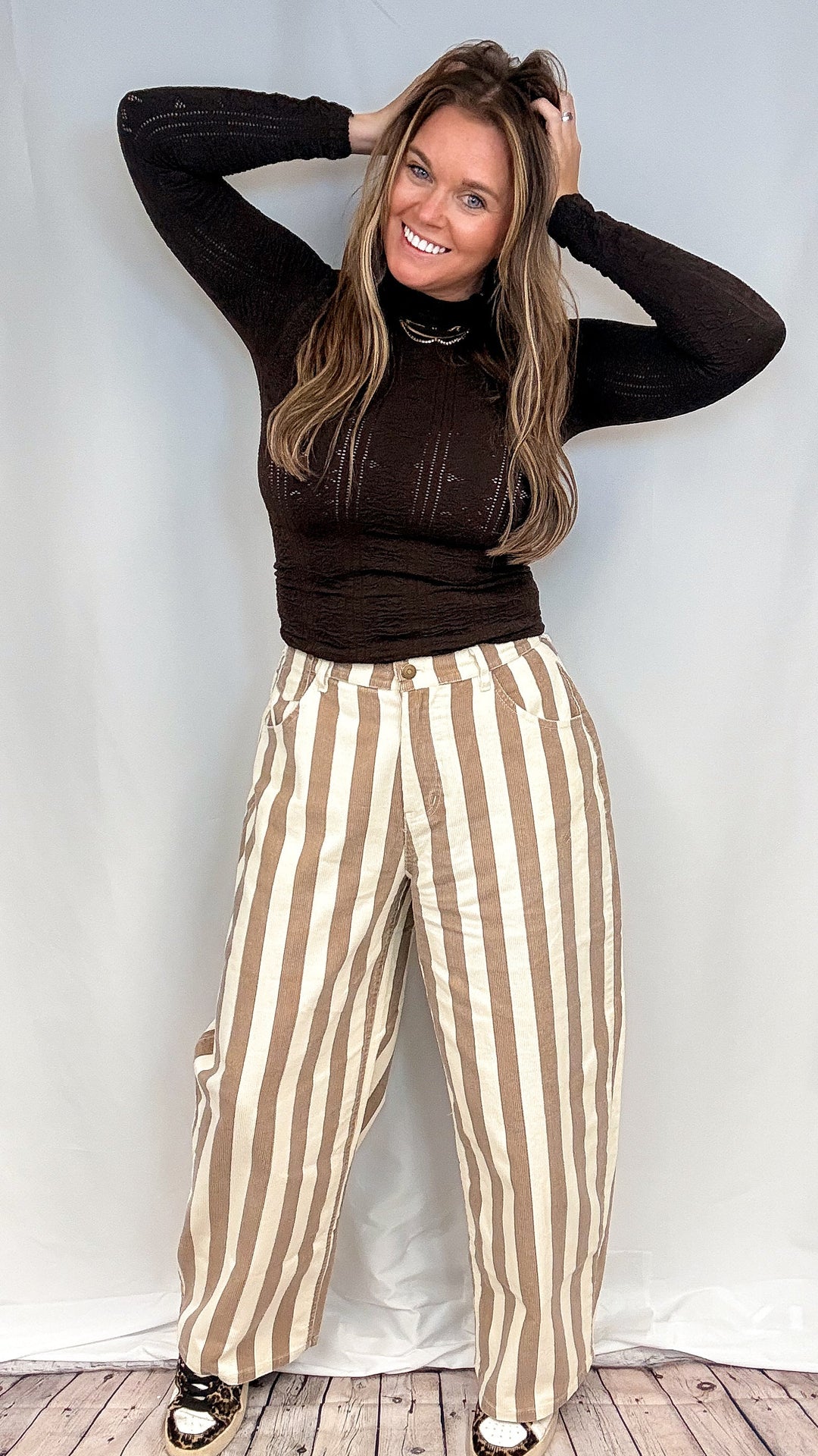 Woman wearing beige and white stripe pants and brown mock neck top on white background
