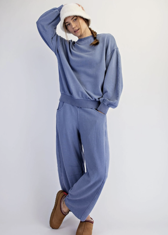 Woman wearing dusty blue matching sweat set with white bucket hat and slippers on plain background