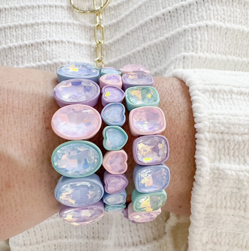 Close up of a hand wearing three pastel bracelets with gemstones over a cream sweater.