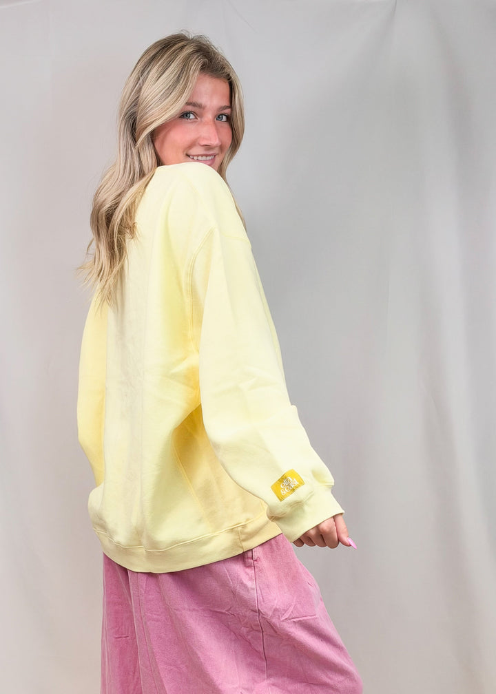 A woman modeling a pale yellow oversized long-sleeve top and pink wide-leg pants against a light gray studio backdrop.